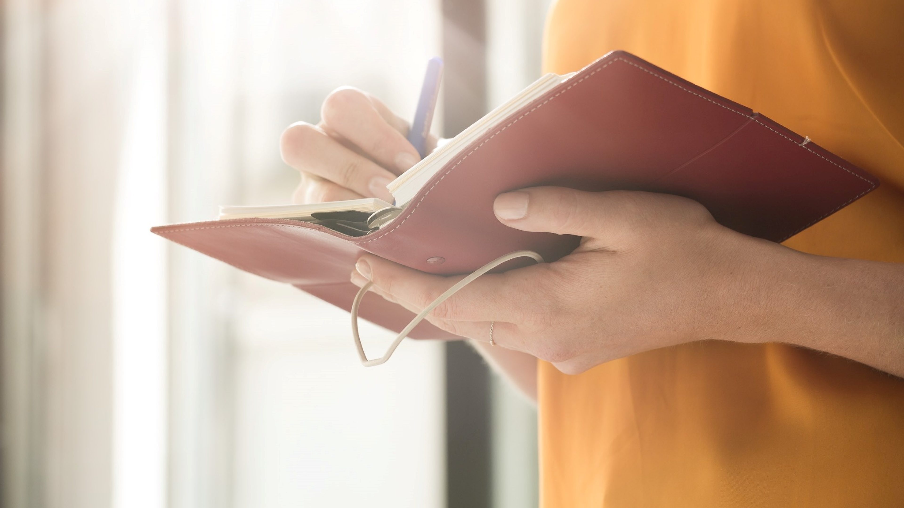 Hands of a women holding a red notebook and writing with a pen